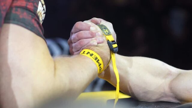 strong male hands and palms locked in a fierce struggle at hand wrestling competitions, fastened with a yellow belt for fixation