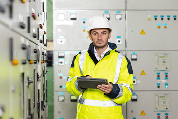 Man electrical engineer hold tablet monitoring electrical system in control room. Technician inspect to control panel screen system for generate electricity of factory in manufacture industrial