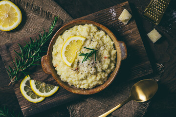 Lemon rice risotto with rosemary and fresh lemon slices on dark wooden background, top view