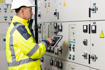 Asian man electrical engineer hold tablet monitoring electrical system in control room. Technician inspect to control panel screen system for generate electricity of factory in manufacture industrial
