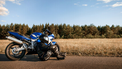 Obraz premium Motorcycle driver in helmet and leather jacket sits on the asphalt road next to a sports motorcycle