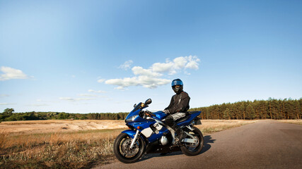 Fototapeta na wymiar Biker man on a motorcycle in a leather jacket and helmet looks at the road