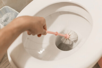 The guy's hand holds the toilet brush and cleans the toilet. The concept of home cleaning and hygiene in the bathroom