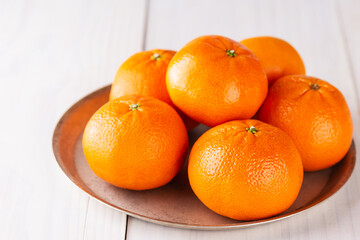 Fresh tangerines in a plate on a wooden table.