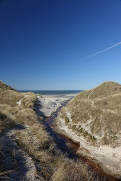 Small river opening out into the North Sea in the dunes of Blokhus on a sunny day, Jammerbugt, Northern Jutland, Denmark
