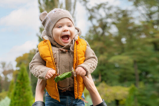 A Small Baby Throwing In The Air Outdoors In Autumn Park. Mom Throws Her Little Smiling Baby Up In The Sky. Happy Family