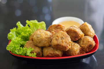 Deep Fried Crab Meat Rolls or Thai name is Hoi Jo in red plate with vegetables and  plum sauce on black table.