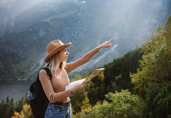 Wanderlust and travel concept. Stylish traveler girl in hat looking at map, exploring woods.