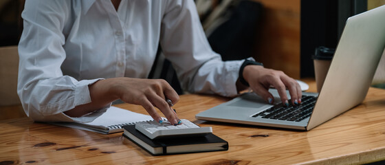 Close up accountant woman working about financial and analysis business document with calculator and holding glasses at his office to calculating expenses, Accounting concept.