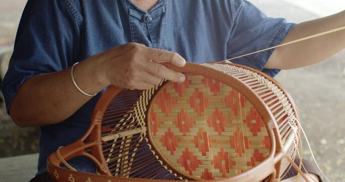 Cut in shot of Thai female farmer weave basket in traditional Thai art patterns to sell as extra income in countryside of Thailand.