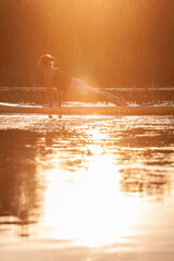 Woman doing yoga on sup board on sunset. Outdoor summer activity. Vertical image