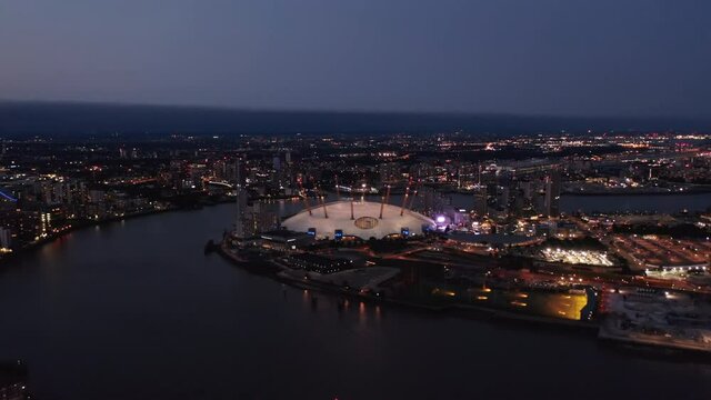 Evening aerial view of Millennium Dome. O2 arena at night. Illuminated city streets and buildings. London, UK