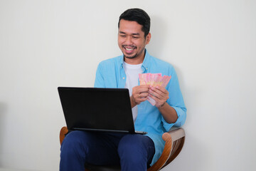 Adult Asian man showing happy expressin while counting money that he earn