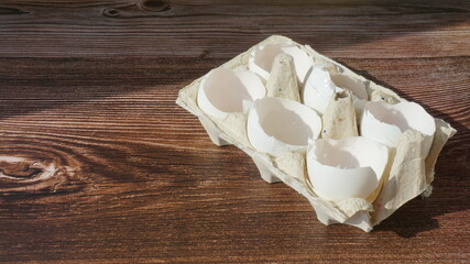 shells of broken white chicken eggs in a cardboard tray on a wooden surface sun rays breakfast