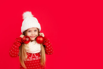 a child girl with Christmas tree balls as earrings on her ears on a red monochrome isolated...