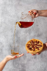 Pecan pie tea party. Creative shot of pouring tea. Female hand pouring tea from glass teapot into cup on concrete gray background.