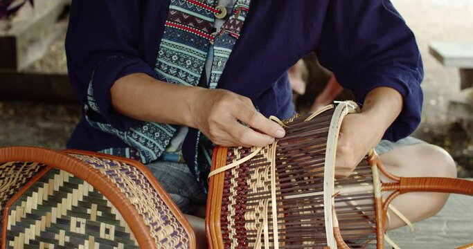 Cut in shot of Thai female farmer weave basket in traditional Thai art patterns to sell as extra income in countryside of Thailand.