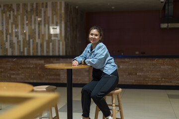 girl in blue denim clothes sitting on a high bar stool in a cafe and posing for the camera, relaxed mood