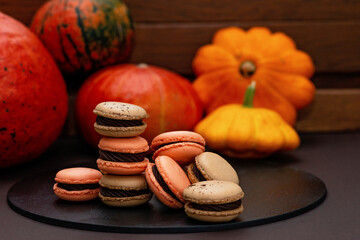Dessert for Halloween. Thanksgiving menu. French macarons. Macaroons with chocolate on a stone pastry board against a black background with pumpkins. Soft selective focus.