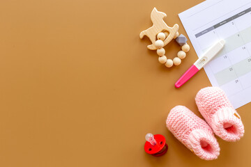 Pink baby girl booties with pregnancy test on calendar, top view