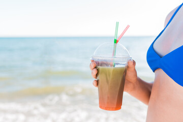 A young girl teenager holds and drink a colored cold non-alcoholic cocktail in her hand against the background of the sea beach