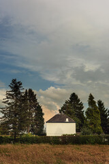 White country house among trees in a field under a blue cloudy sky.