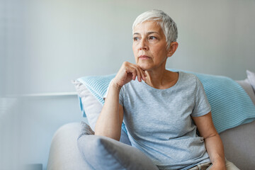 Pensive thoughtful middle aged lady looking away sit alone at home feel anxious lonely, sad depressed melancholic old mature woman suffer from sorrow grief thinking of problem suffer from solitude - obrazy, fototapety, plakaty