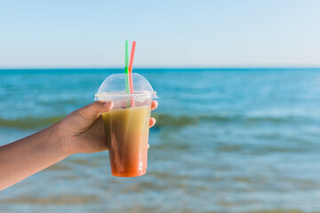 The guy's hand holds a colored chilled non-alcoholic cocktail against the background of the sea