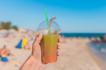 The guy's hand holds a colored chilled non-alcoholic cocktail against the background of the sea beach