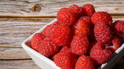 a white bowl with ripe raspberries on a wooden surface summer is sunny