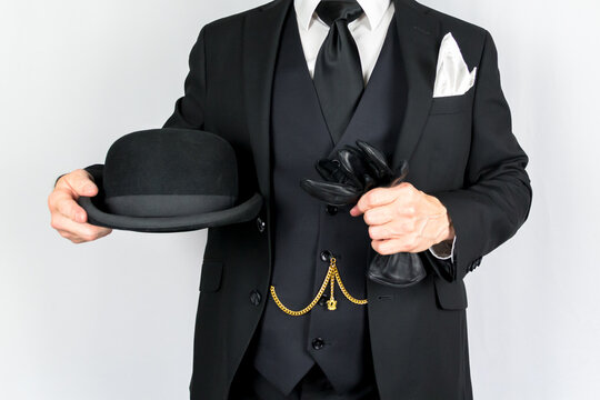 Portrait of Man in Dark Suit Holding Bowler Hat and Leather Gloves on White Background. Vintage Style and Retro Fashion of Classic British Gentleman.