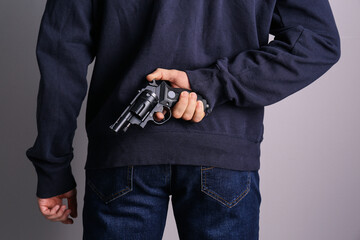 Man holding gun behind his back on grey background, closeup