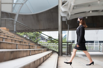 A woman wearing a black suit and skirt, she is walking up the stairs.