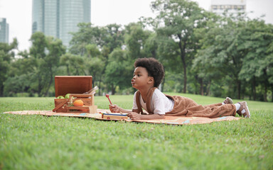 Happy little African boy lying down on mat and playing xylophone toy at garden. African family...