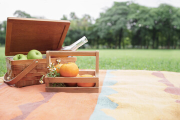 Selective focus on oranges and little flowers in wooden basket and basket of green apples and drinks in glass bottle place on color mat in green park at sunny day. Copy space