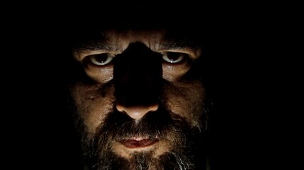 Bearded man in the dark looking at the camera. Low light in the dark.