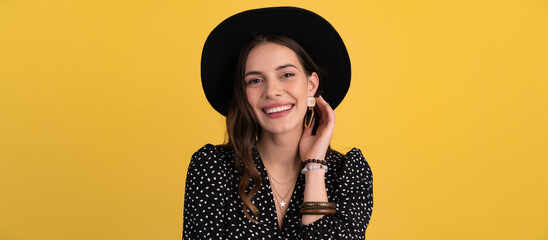 attractive woman posing isolated on yellow background wearing black hat and dress