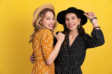 beautiful women friends together isolated on yellow background in black and yellow dress and hat