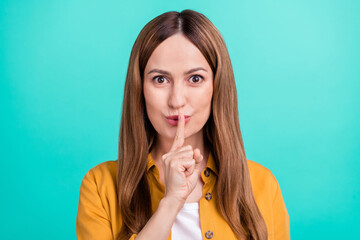 Photo of serious confident young woman dressed yellow shirt smiling finger lips asking keep silence isolated teal color background