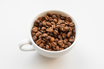 A white cup filled with brown coffee beans on white background