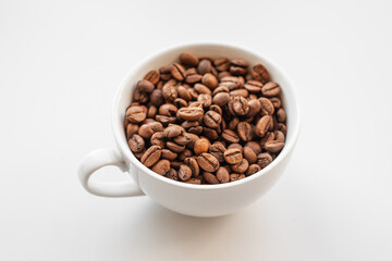 A white cup filled with brown coffee beans on white background