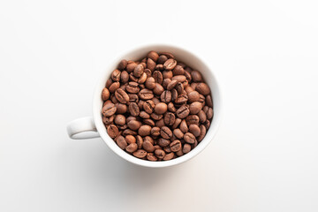 A white cup filled with brown coffee beans on white background