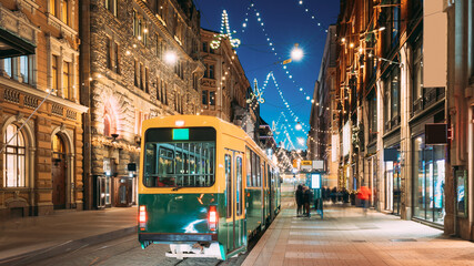 Helsinki, Finland. Tram Departs From Stop On Aleksanterinkatu Street. Night Evening Christmas Xmas New Year Festive Illumination On Street. Beautiful Street Decorations During Winter Holidays - obrazy, fototapety, plakaty