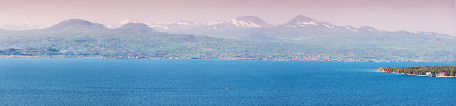 Panoramic view of famous Sevan lake with high mountain ranges with snow capes. Dramatic and scenic highland landscape. Tourist attractions in Armenia