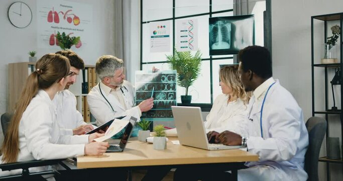Medical council concept where good-looking confident qualified diverse medical workers discussing results of patient's x-ray scan and advicing about further treatment