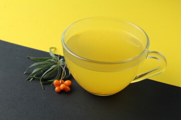 sea buckthorn tea drink on a bright background. Sea buckthorn drink tea juice in a glass cup next to a spout of sea buckthorn leaves orange berries on a black and yellow background. Seasonal berry