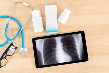 Medication, tablet, x-ray and stethoscope on wooden desk. Doctor workplace.