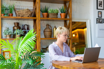 Woman in eyeglasses works with documents in front of a laptop monitor in home interior. She checking the tax forms.