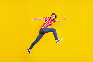 Fototapeta na wymiar Photo of funky pretty young guy dressed red t-shirt jumping high running fast smiling isolated yellow color background