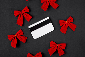 Credit card blank and red festive bow decorations on black. Christmas and New Year shopping. Sales and discounts on winter holidays